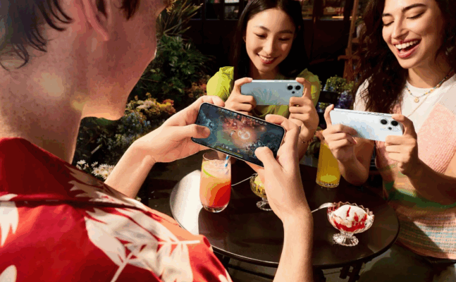 กลุ่มเพื่อน 3 คนกำลังเล่นเกมมือถือบนสมาร์ทโฟน OPPO Reno14 Pro (หรือรุ่นที่ใกล้เคียง) เพื่อเน้นประสิทธิภาพด้านเกมมิ่งในการเปรียบเทียบ OPPO Reno14 Pro vs vivo V60