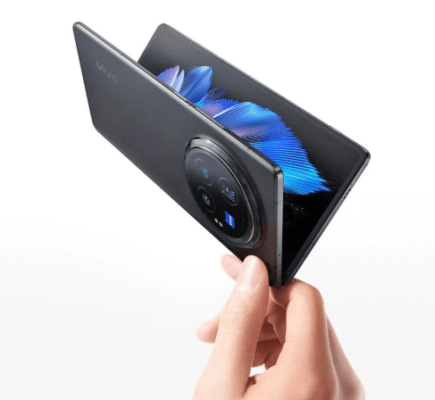 มือที่กำลังถือสมาร์ทโฟนพับได้ Vivo X Fold5 สีดำ-เทาเข้ม ในลักษณะกางออกเพียงเล็กน้อย โดยเน้นไปที่โมดูลกล้องขนาดใหญ่และหน้าจอที่แสดงวอลล์เปเปอร์สีน้ำเงินสดใส เหมาะสำหรับประกอบบทความ Vivo X Fold5 Review