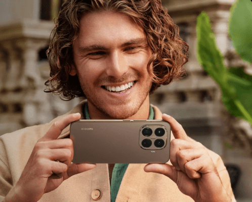 รูปภาพชายหนุ่มยิ้มแย้มถือ Xiaomi 15T Pro สีน้ำตาลในแนวนอนเพื่อถ่ายภาพ เน้นการใช้งานในการ รีวิว Xiaomi 15T Pro