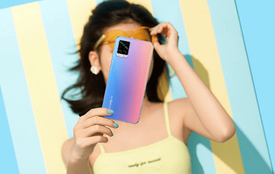 vivo มือถือแต่ละซีรีส์ต่างกันอย่างไร ภาพผู้หญิงถือสมาร์ทโฟน vivo ดีไซน์สีพาสเทลไล่เฉดสีฟ้าชมพู นอนเล่นอยู่บนผ้าเช็ดตัวลายทางสีเหลืองฟ้า เป็นรูปหน้าปกบทความเปรียบเทียบความแตกต่างของมือถือ vivo แต่ละซีรีส์