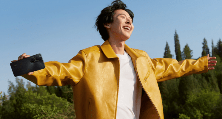 ชายหนุ่มสวมเสื้อแจ็กเกตหนังสีเหลืองสดใส ยืนกางแขนและเงยหน้ายิ้มรับแสงแดดกลางแจ้ง พร้อมถือสมาร์ทโฟนสีดำ ซึ่งเป็นภาพที่แสดงถึงการถ่ายภาพที่สดใสตามหลักวิธีถ่ายรูปสวยด้วย HUAWEI