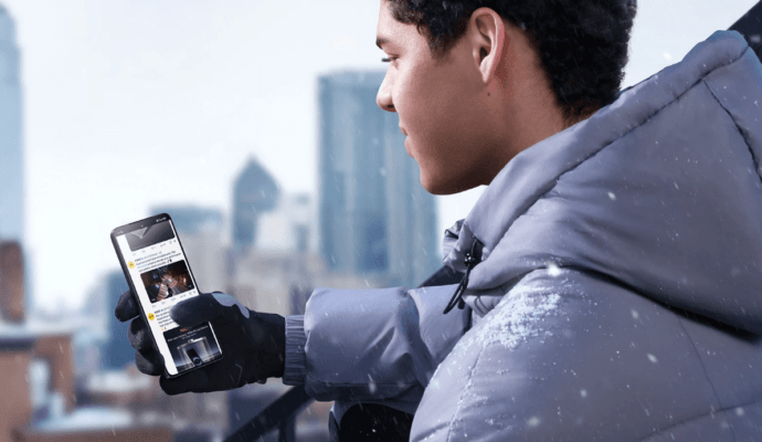 รีวิว POCO F7 PRO: ชายหนุ่มใส่เสื้อกันหนาวกำลังใช้สมาร์ทโฟน POCO กลางหิมะบนตึกสูงเพื่อเน้นการใช้งานในทุกสภาพอากาศ"