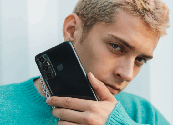 $Redmi\ vs\ Infinix$: ชายหนุ่มถือโทรศัพท์มือถือสีดำให้เห็นดีไซน์ด้านหลังและชุดกล้องอย่างชัดเจน