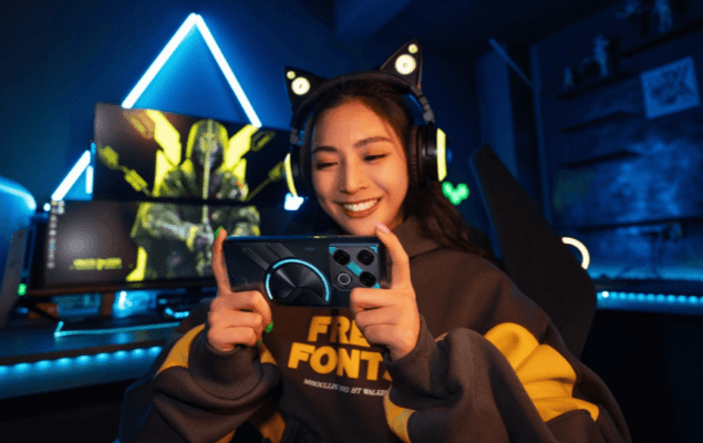 ภาพหญิงสาวเกมเมอร์ (Gamer) กำลังเล่นเกมอย่างสนุกสนานบนโทรศัพท์มือถือ Infinix GT Series ที่มีดีไซน์ฝาหลังแบบ Cyber-Mecha ที่โดดเด่น ในห้องเล่นเกมที่มีแสงไฟสีน้ำเงินนีออน ภาพนี้แสดงถึงประสิทธิภาพการเล่นเกมของ Infinix ซึ่งเป็นคู่เปรียบเทียบในบทความ TECNO vs Infinix