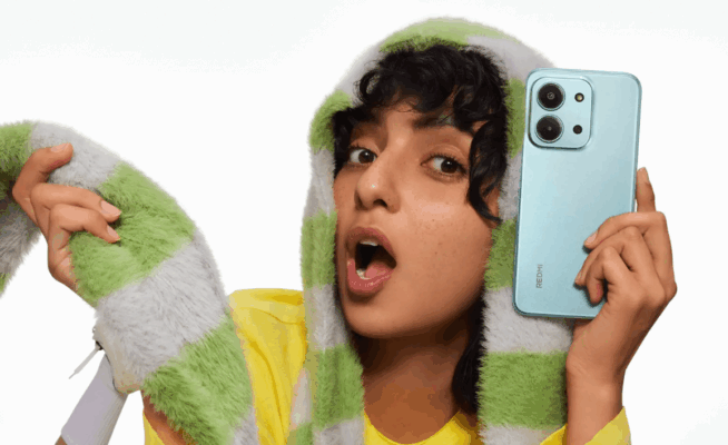 รูปหญิงสาวผิวสีแทนกำลังถือสมาร์ทโฟน Redmi สีฟ้าอ่อน โชว์กล้องด้านหลัง พร้อมทำท่าทางตกใจ (หรือประหลาดใจ) ด้วยชุดที่ดูแฟชั่น เหมาะสำหรับบทความ วิธีถ่ายรูปสวยด้วย Redmi
